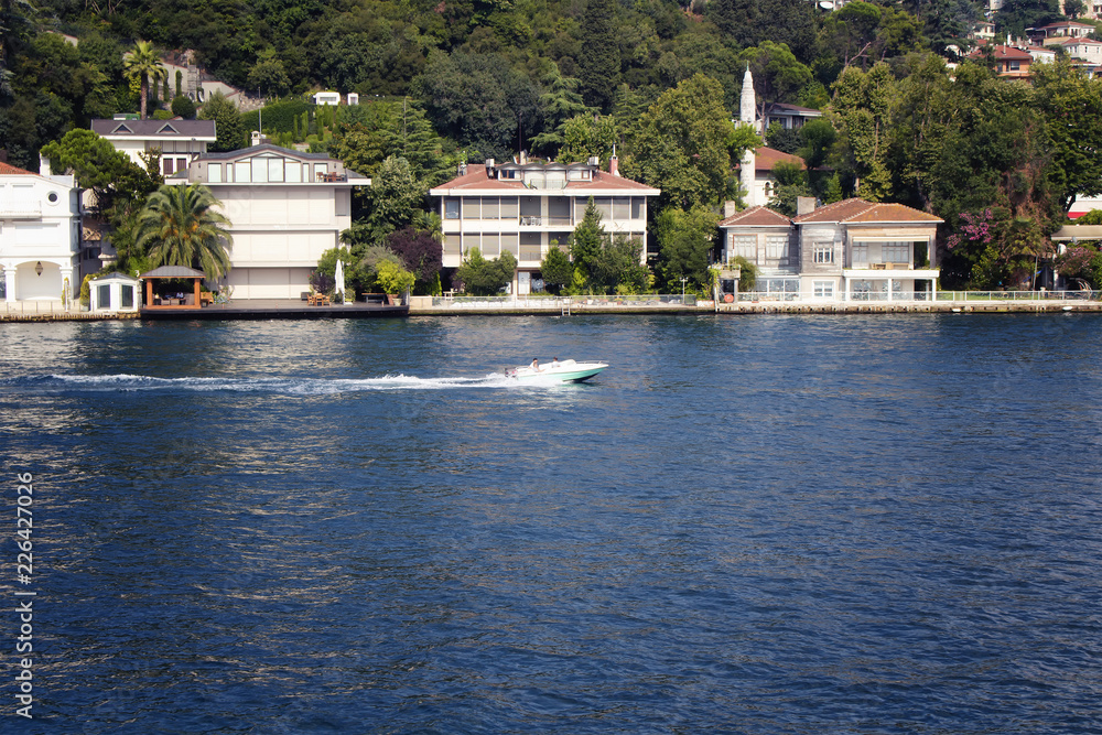 View of small motorboat on Bosphorus, houses on Asian side of Istanbul. It is a sunny summer day.