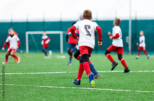 football teams - boys in red, blue, white uniform play soccer on the green field. boys dribbling. dribbling skills. Team game, training, active lifestyle, hobby, sport for kids concept 