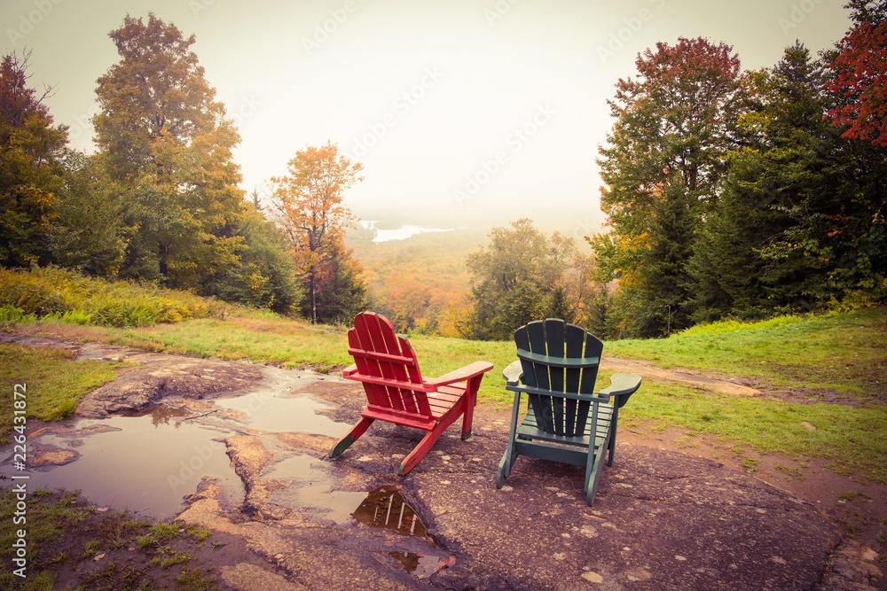 Two empty adirondack chairs overlook a foggy valley with fall color