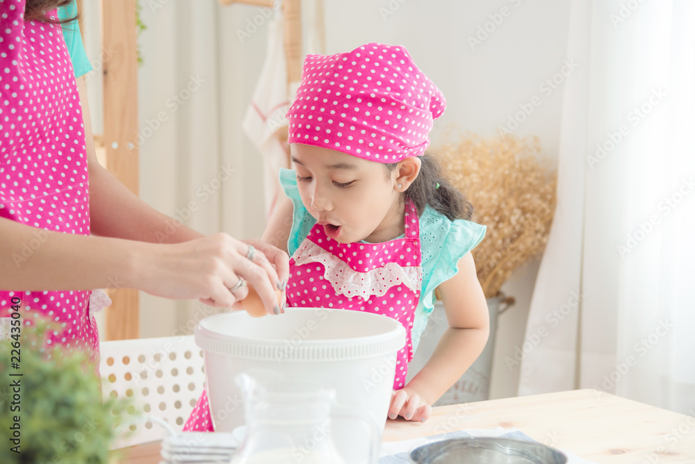 Mother and daughter wearing pink apron making cake in the kitchen. Mother and daughter wearing pink apron making cake in the kitchen.