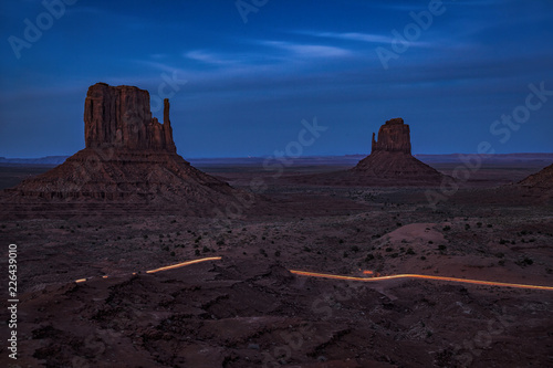 Long exposure of a car driving by the Mittens of Monument Valley at twilight