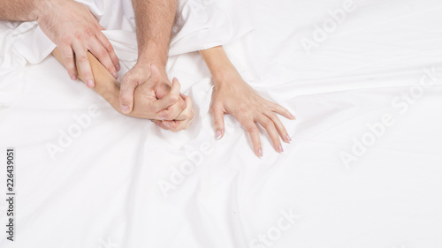 Four hands on the linens. Couple having sex on the bed.