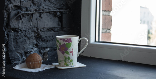 a cup with tea and cupcake near the window photo