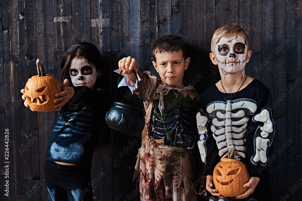 Three cute kids in scary costumes during Halloween party in an old house.
