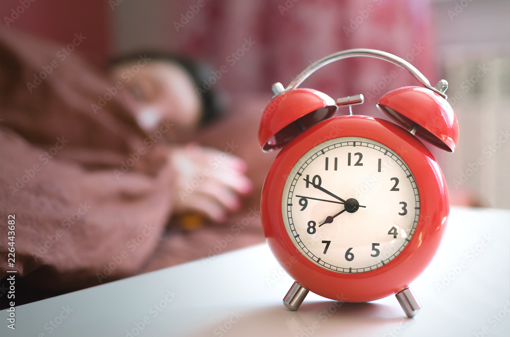 Sleepy woman in the bed and a red alarm clock with eight o clock on the table at morning time. Sleepy woman in the bed and a red alarm clock with eight o clock on the table at morning time.