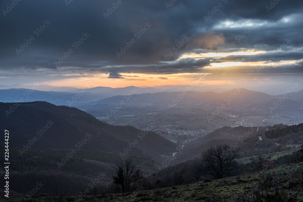 Sunrays coming over a valley in Umbria (Italy) with some plants in the foreground