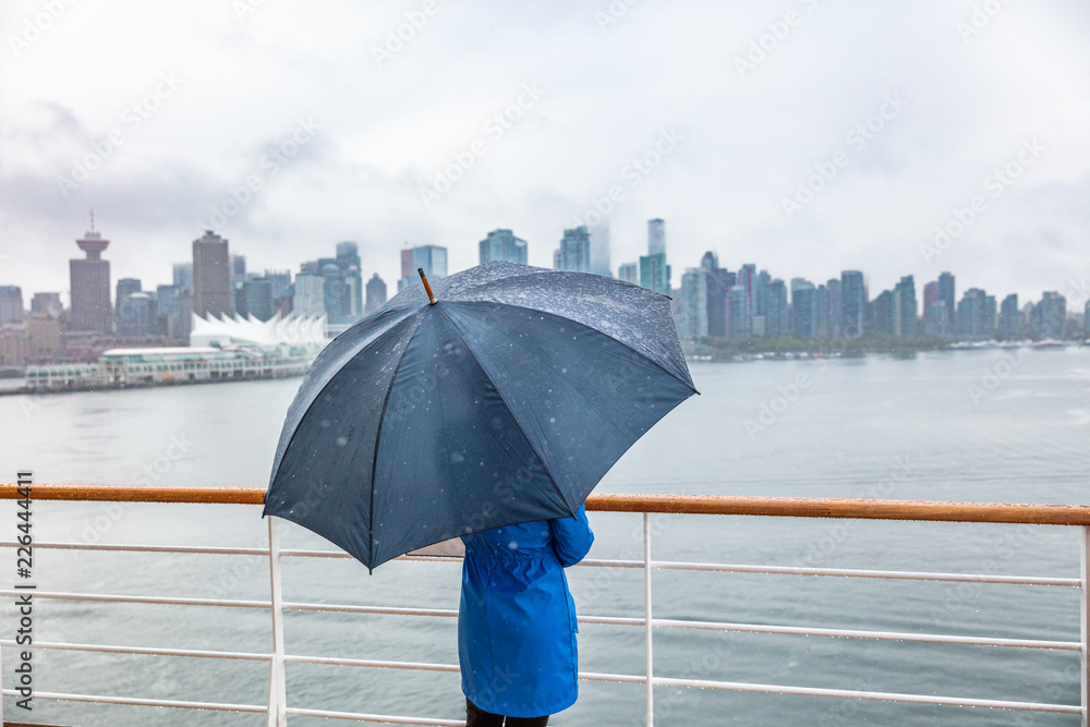 Naklejka premium Luxury travel cruise woman leaving port watching city skyline of Vancouver under the rain with umbrella. Ship voyage destination in autumn.