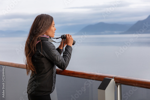 Alaska cruise woman on whale watching boat excursion tour looking at wildlife with binoculars. Tourist at inside passage Glacier Bay destination on travel ship vacation enjoying scenic cruising.