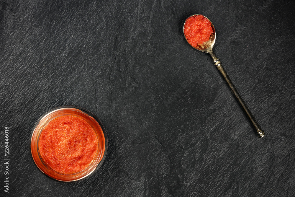 An overhead photo of red caviar in a jar and in a spoon, shot from above on a black background with a place for text An overhead photo of red caviar in a jar and in a spoon, shot from above on a black background with a place for text