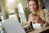 Businesswoman using smartphone in front of laptop, sitting at coffeeshop