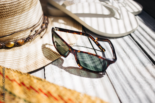 A hat, white flip flops, sunglasses, a beach bag on the white wooden background, hard light