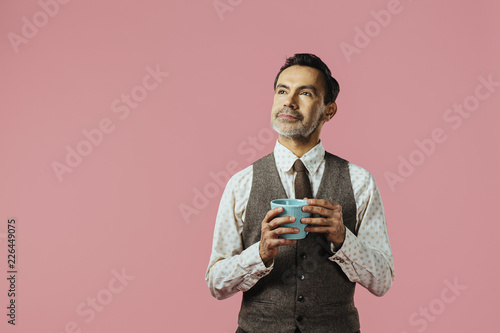 Portrait of a mature man holding coffee cup and looking up, isolated on pink studio background © Carlos David