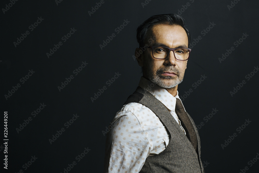 Fototapeta premium Close up portrait of a mature man in brown vest and tie looking at camera, isolated on black studio background