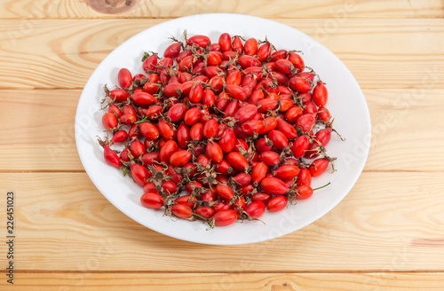 Dried red rose hips on white dish on wooden surface