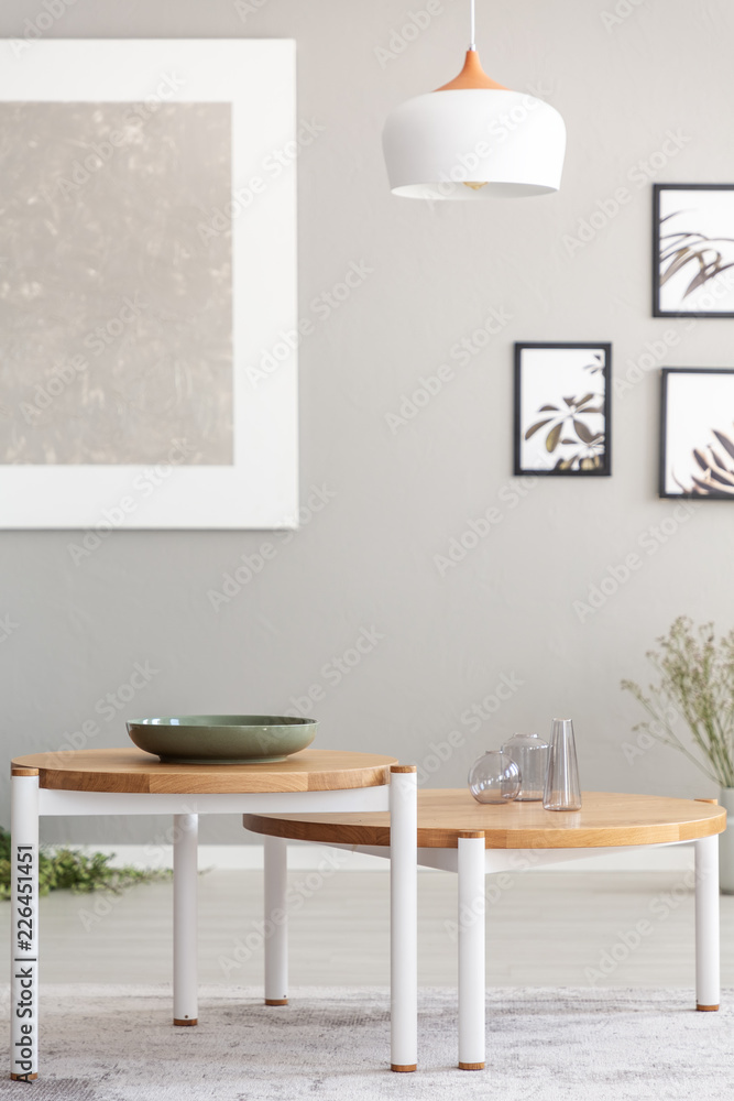 Lamp above wooden tables in grey living room interior with posters and mockup. Real photo Lamp above wooden tables in grey living room interior with posters and mockup. Real photo