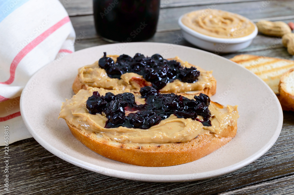 Toasts with peanut butter and berry jam on a plate on a wooden table. Nutritious breakfast. Traditional american food. Toasts with peanut butter and berry jam on a plate on a wooden table. Nutritious breakfast. Traditional american food.