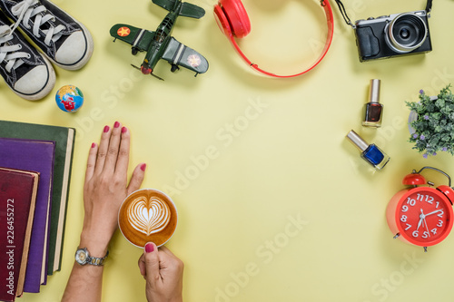 Yellow wooden table with woman hands holding cup of coffee,headphone,camera and alot of thing.Top view with copy space.