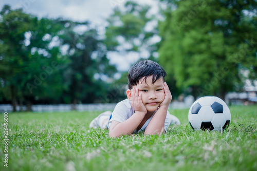 Little Asian child playing football and celebrating on grass.