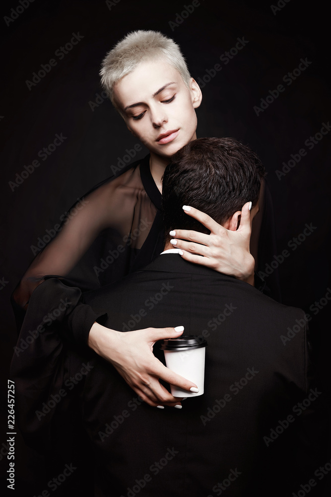 Girl with short hair hugs a guy with coffee on a black background. Passion. Creative advertising. Girl with short hair hugs a guy with coffee on a black background. Passion. Creative advertising.