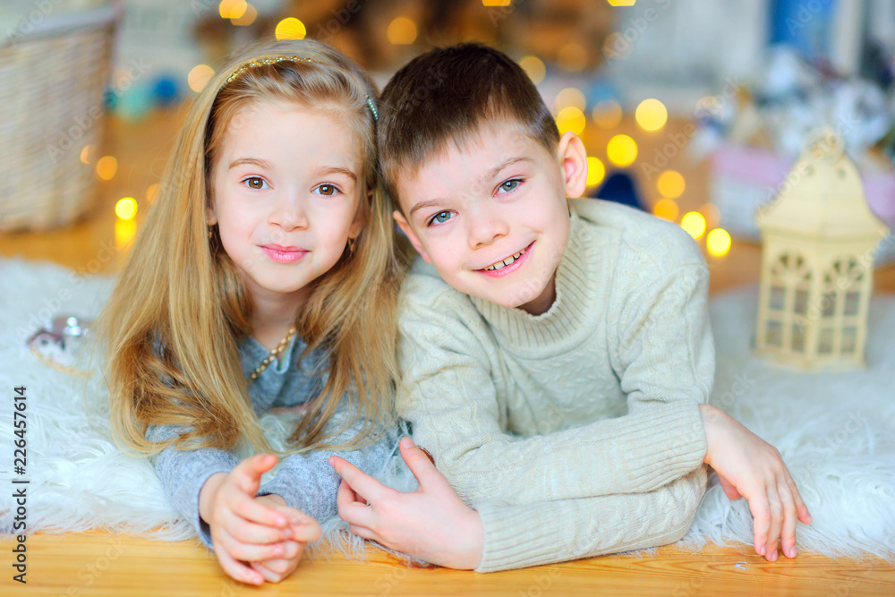 brother and sister lie on the floor amid a bright festive background