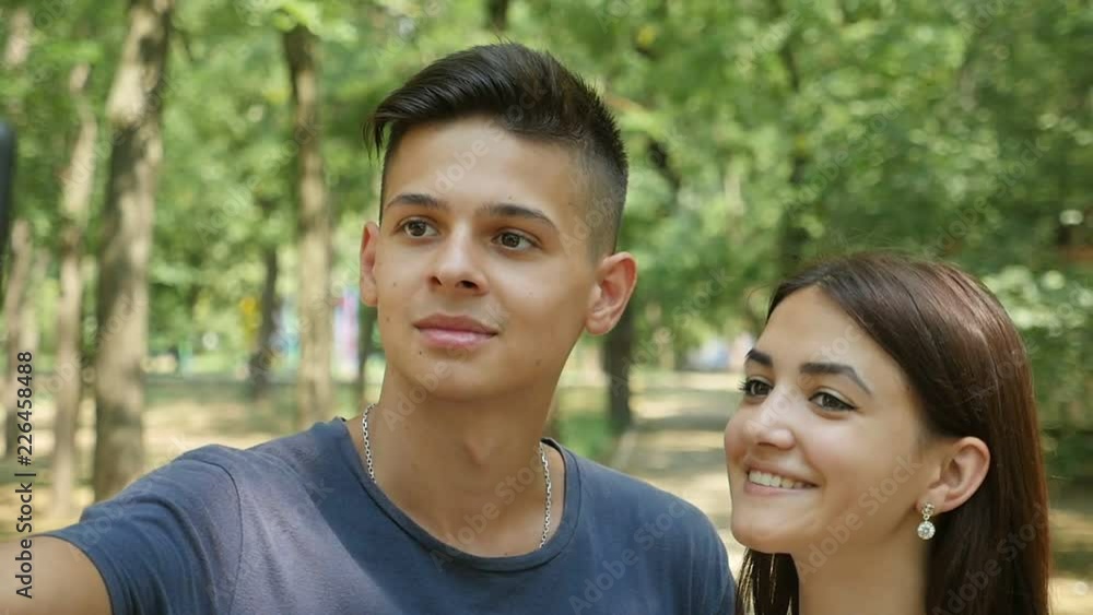 Astonishing view of an inspired young man taking a selfie with his cutie brunet girl smiling nearby emotionally in a green wood Astonishing view of an inspired young man taking a selfie with his cutie brunet girl smiling nearby emotionally in a green wood