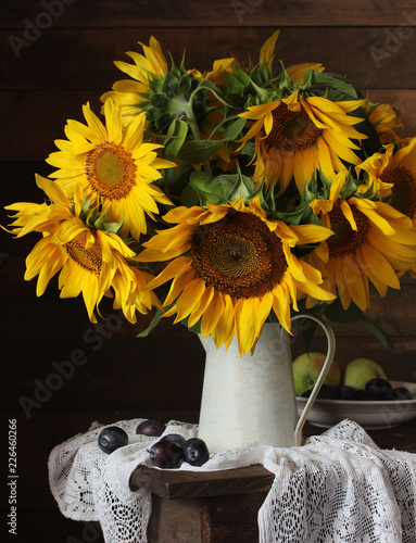 Still life with a bouquet of yellow sunflowers, plums and apples.