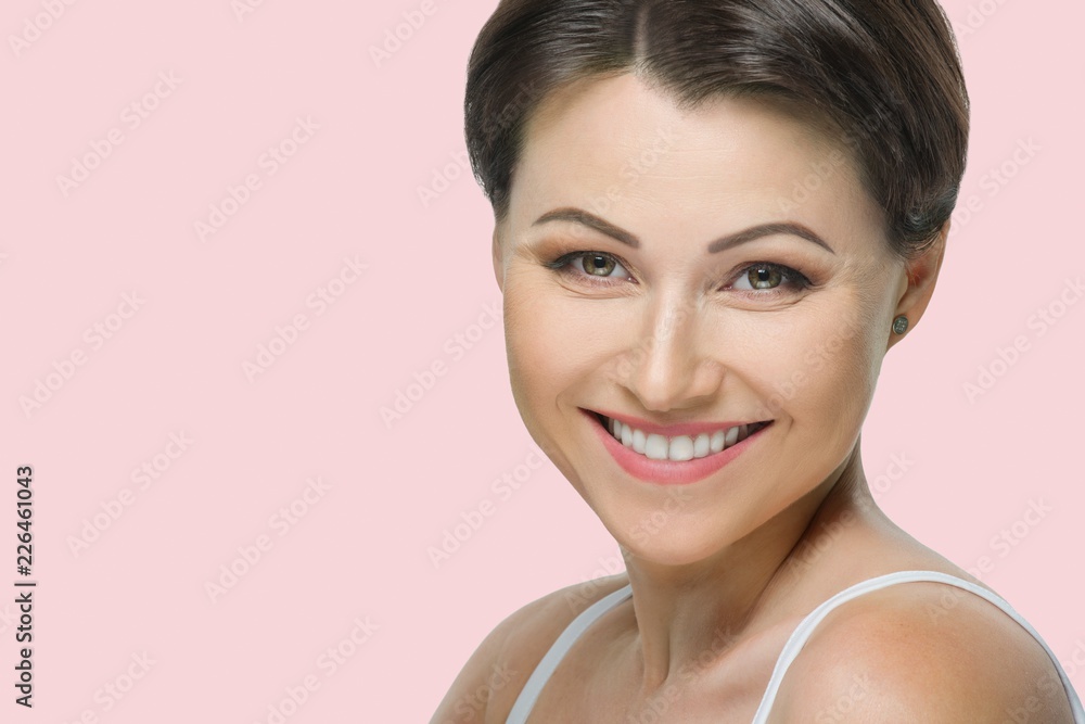Positive mature brunette woman with beautiful white smile close up on pink pastel background Positive mature brunette woman with beautiful white smile close up on pink pastel background