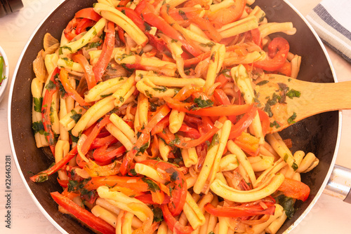 Italian vegetarian food - Pasta with peppers and onions in a pan close-up, top view