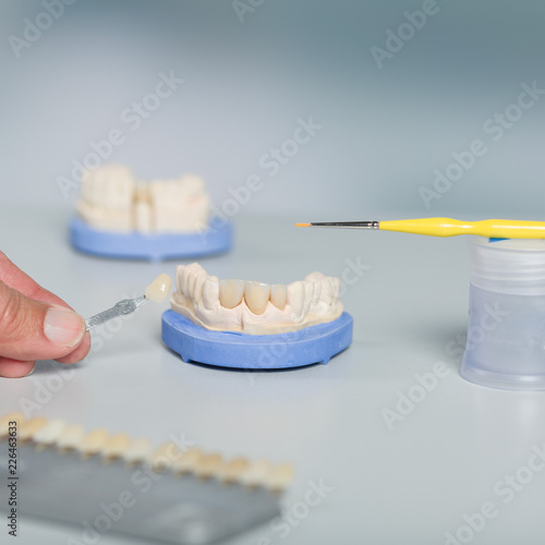 Hand mit Zahnfarbprobe am Zahnersatz im Dentallabor mit Pinsel