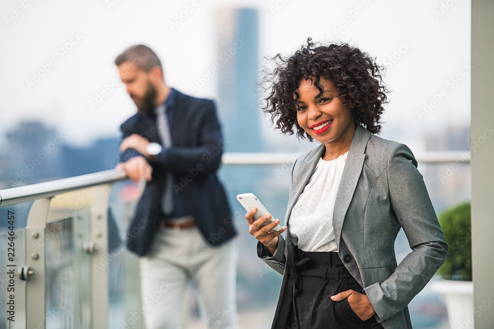 A portrait of a businesswoman with smartphone standing on a terrace. A portrait of a businesswoman with smartphone standing on a terrace.