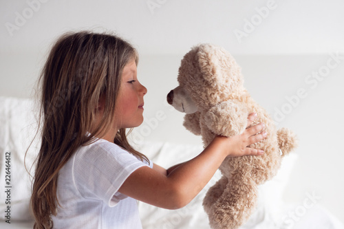 Portrait of a young girl while she is playing with her teddy bear on the bed. © Kitreel