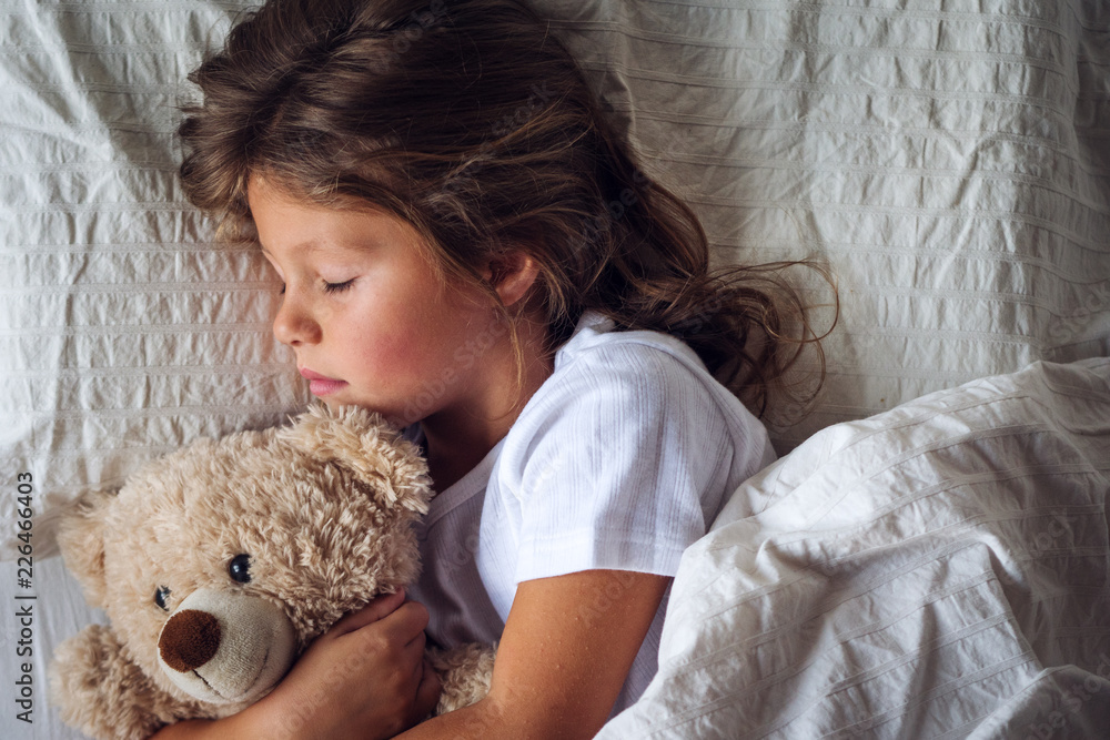 Portrait of a young girl (kid) sleeping in her bed and hugs a teddy bear. Portrait of a young girl (kid) sleeping in her bed and hugs a teddy bear.