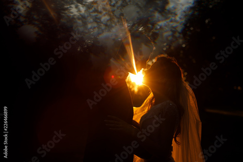 Evening light sparkles behind kissing wedding couple in the park