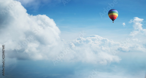 Colorful hot air balloon flying against blue cloudy sky.