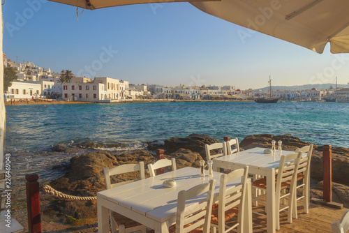 Chairs with tables in typical Greek restaurant  of Mykonos old town, Cyclades island, Greece.panoramic view of the marina, the sandy beach and the characteristic white houses. © vololibero