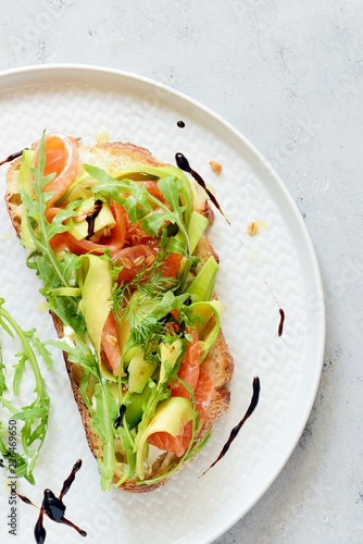 Brusctta with avocado, salmon, fresh leaves of arugula and balsamic. Breakfast with fresh organic greens, snacks, gravlax photo