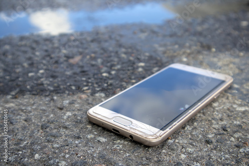 Modern smart phone with cracked screen glass lying in a puddle on the wet asphalt