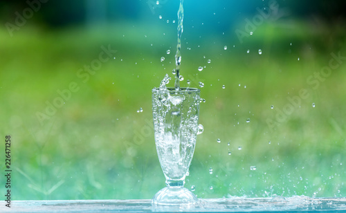 Drink water pouring in to glass over sunlight and natural green background.Select focus blurred background.Fresh Clean water splash. © noon@photo