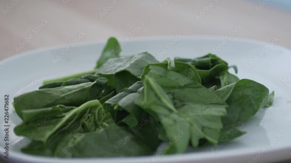 Large green leaves of spinach slowly fall on the plate. Female hand rips spinach for salad and puts it in the plate. Then mix the spinach by hand. Large green leaves of spinach slowly fall on the plate. Female hand rips spinach for salad and puts it in the plate. Then mix the spinach by hand.