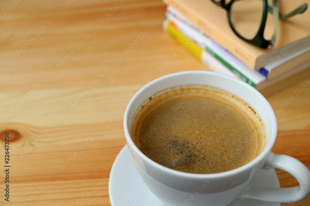 A cup of hot coffee with stack of book and glasses on the wooden table A cup of hot coffee with stack of book and glasses on the wooden table