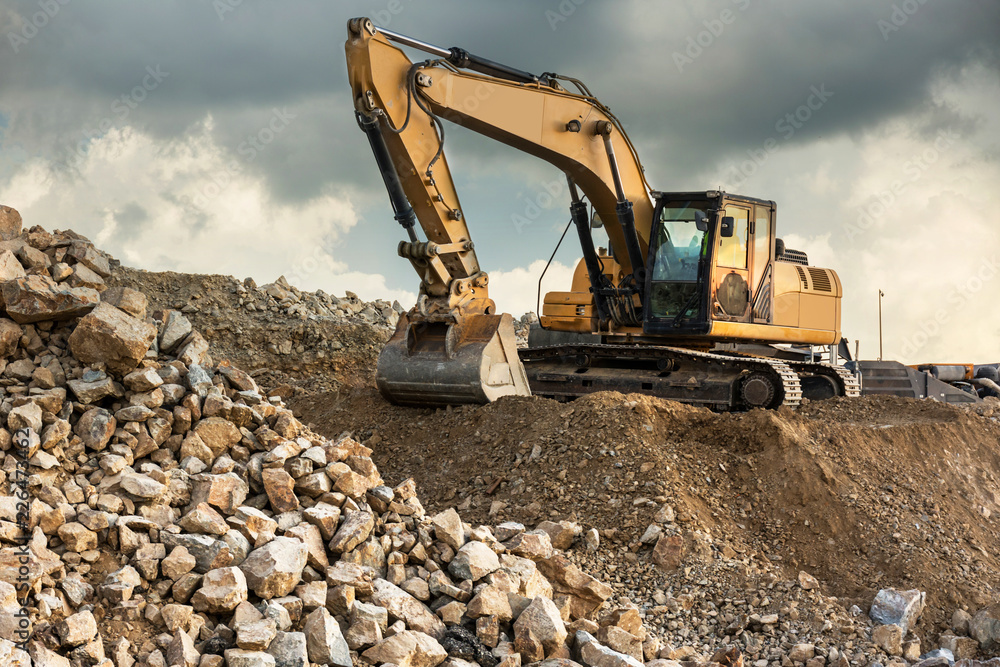 A large yellow excavator moving stone in a quarry A large yellow excavator moving stone in a quarry
