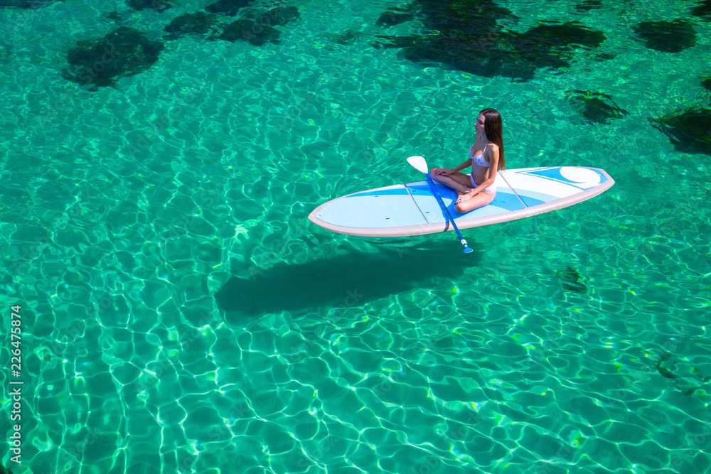 Young beautiful woman in a bikini on a SUP board in the sea.Young attractive woman meditating on the sup board in the sea. Girl in meditative pose on water.