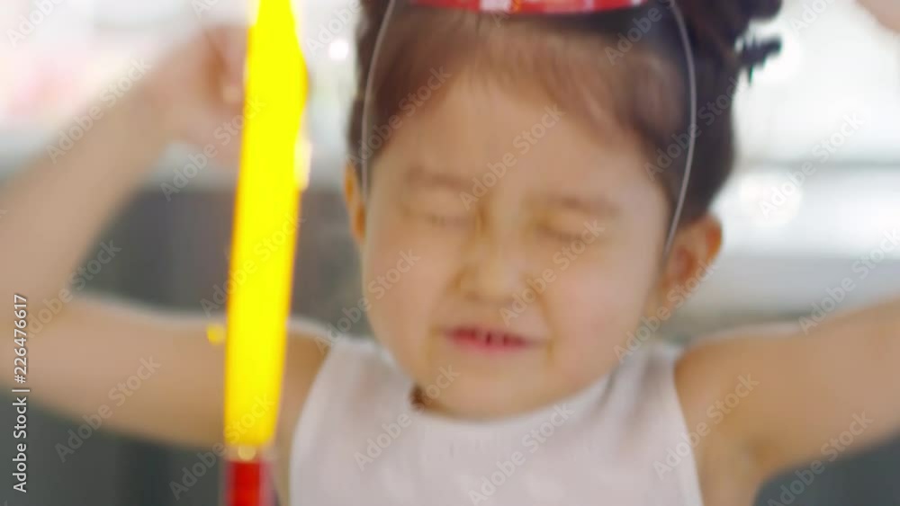 Dolly shot of adorable Asian girl in party hat celebrating before birthdate cake with firework candle Dolly shot of adorable Asian girl in party hat celebrating before birthdate cake with firework candle