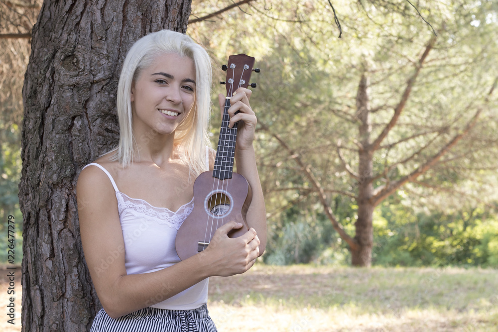 Attractive young woman playing ukulele in the field
