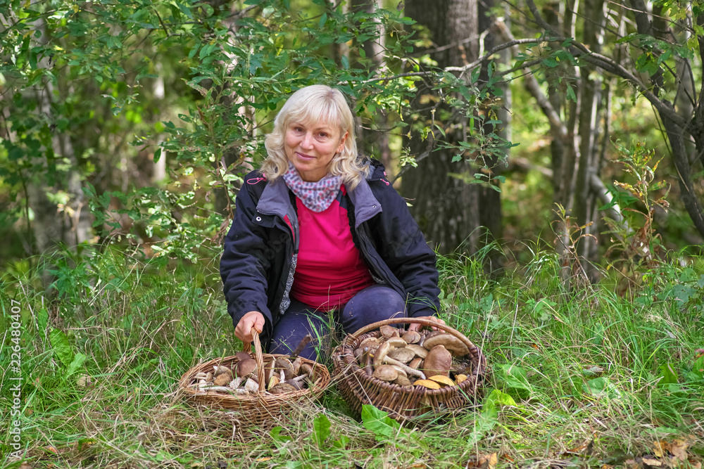 A beautiful middle-aged blonde in a forest with two baskets of mushrooms looks into the camera A beautiful middle-aged blonde in a forest with two baskets of mushrooms looks into the camera