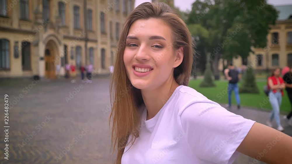 cute caucasian girl is smiling chill at camera and looking straight in motion, city view, street, daytime cute caucasian girl is smiling chill at camera and looking straight in motion, city view, street, daytime
