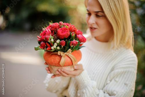 Blonde girl holding a pumpkin decorated with red flowers