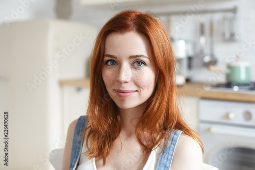 Free Download Headshot of charming beautiful young European woman with red shiny hair and freckles cooking or having meal in kitchen interior, looking at camera with cute smile. People and lifestyle concept - GFXLoad