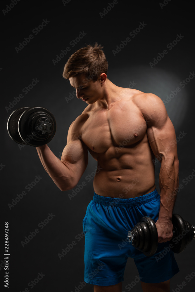 Strong bodybuilder with perfect deltoid muscles, shoulders, biceps, triceps and chest. Close up power fitness man. Handsome power athletic man in training swap muscles with dumbbells. Black background