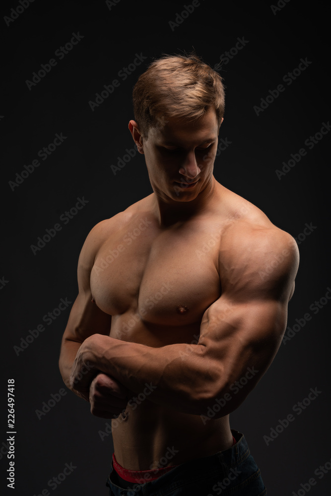 Fototapeta premium young, Strong bodybuilder with six packs. Bodybuilder flexes muscles against dark background